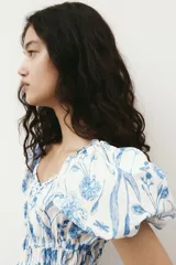 Vestido corto blanco con estampado floral azul, escote cuadrado con volados, mangas cortas abullonadas con elástico y cintura elastizada.