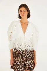 Blusa blanca con escote en V y mangas tres cuartos abullonadas. Presenta bordados y calados en el escote, mangas y ruedo. Cierre frontal con botones.