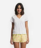 Pijama corto de algodón con blusa blanca de cuello V con botones y mangas cortas onduladas, y short amarillo con estampado de corazones y cintura elástica.