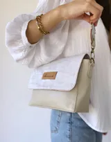 Bandolera color crudo con solapa de gamuza y cuerpo de cuero sintético texturizado. Tiene correa corta de cuero con tientos y forro de tela con bolsillo interno.