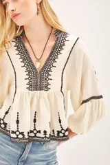 Blusa negra de viscosa crepe con escote en V, mangas largas con terminaciones elásticas y bordado de hilo color crema.
