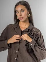 Camisa de corte clásico, color marrón oscuro con brillo sutil dorado, confeccionada en tela nacarada. Presenta apliques de flores tridimensionales fruncidas en el área del pecho.