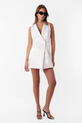 Minivestido blanco tipo blazer sin mangas, con cuello solapa, doble botonadura cruzada, bolsillos ojal y tira de ajuste en la espalda.