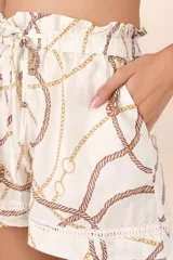 Short de tiro alto color blanco marfil con pretina fruncida ajustable con lazo. Presenta un estampado náutico de cuerdas y cadenas en tonos marrón y dorado. El ruedo tiene un detalle de tira bordada blanca.