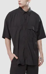 Camisa negra de manga corta con doble bolsillo ojal en delantero, realizada en tejido plano y silueta oversize.