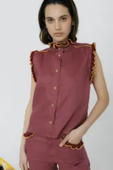 Blusa color borgoña sin mangas con cuello alto y volados en cuello, sisas y bolsillos. Cierre frontal con botones.