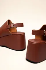 Sandalias con plataforma color marrón, con capellada envolvente, pulsera trasera ajustable y hebilla metálica.