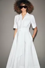 Vestido midi camisero color ladrillo, confeccionado en popelina de algodón. Presenta cuello solapa, manga corta con puños abotonados, bolsillos laterales ocultos y bolsillos de parche con solapa en el pecho. Incluye cinturón lazada en el mismo tejido y cierre frontal con botones ocultos.