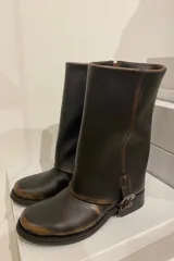 Bota de cuero color marrón oscuro con efecto desgastado, caña media, hebilla lateral y suela plana.