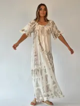 Vestido largo color beige con estampado tie-dye en tonos rosados, corte amplio, mangas cortas con volados y ruedo con flecos.
