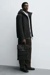 Mochila negra de tejido técnico con solapa y hebilla. Tiene un bolsillo frontal, un bolsillo interior con cierre y un compartimento para dispositivos electrónicos de hasta 13 pulgadas. La parte posterior es acolchada y tiene una banda de sujeción para equipaje.