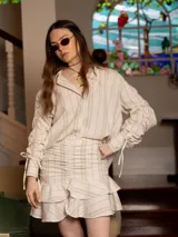 Conjunto de camisa manga larga y falda corta a rayas verticales color beige y blanco. La falda tiene volados y frunces.