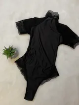 Body entallado de lycra color negro, con detalles en microtul y encaje, cuello alto y espalda descubierta.