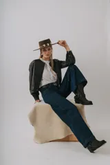 Campera bomber color beige de cuero, con cuello redondo, cierre frontal con botones a presión, mangas largas con puños elásticos y detalles de tachas metálicas en hombros y espalda.