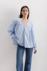 Camisa celeste de algodón con bordado calado, cuello en V y mangas largas abullonadas con puños elásticos.