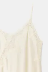 Vestido corto de satén color blanco, con tirantes finos, escote en pico y bajo asimétrico con abertura. Detalle de encaje negro en escote y ruedo.