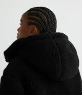 Campera puffer de sherpa color negro, con capucha, cierre frontal y regulador elástico en la cintura.