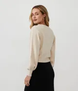 Cardigan corto de punto color crema, con escote en V, abotonadura frontal y mangas largas abullonadas con puños acanalados. Presenta un punto calado en forma de rombos en la parte superior del busto y en las mangas.