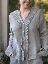 Camisa blanca de lino con cuello mao, mangas largas abullonadas y cierre frontal con botones de nácar. Presenta volados en el frente y puños elásticos.