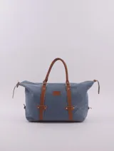 Bolso de viaje azul con textura y detalles en cuero marrón. Tiene doble asa de mano, cierre superior con cremallera, bolsillo interno con cierre y forro interior.