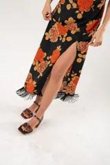 Vestido midi negro con estampado de flores naranjas y beige, espalda descubierta con tres botones en forma de flor, tajo lateral y flecos en el ruedo.