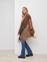 Ruana tejida con diseño colorblock en tonos de gris y beige, con flecos en el borde inferior.