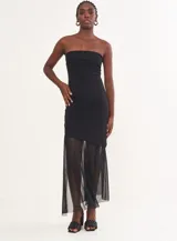Vestido negro strapless con corte ajustado y falda asimétrica con paneles de tul transparente.