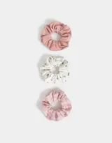 Set de tres scrunchies para el pelo con diferentes estampados: uno liso color rosa, uno blanco con estampado de flores pequeñas y uno a cuadros rosa y blanco.