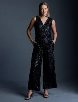 Enterito de lentejuelas marca Ninety, color negro, con escote en V cruzado y diseño sin mangas. Presenta cintura elastizada con lazo de ajuste, bolsillos frontales y abertura en la espalda con cierre invisible. Incluye forro interno a tono.