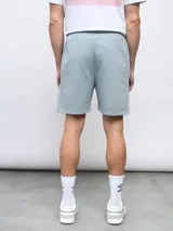 Bermuda gris de felpa sin friza, con cintura elástica ajustable con cordón y logo Umbro estampado en rojo en la pierna izquierda.