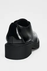 Zapato tipo mocasín negro acharolado con punta redonda y cierre de cordones. Suela de 4 cm de altura.