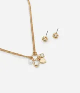 Conjunto de bisutería con baño dorado que incluye un collar de cadena fina y un par de caravanas. El collar cuenta con un dije circular del que cuelgan varios charms: un corazón metálico, una perla de imitación y cristales facetados. Las caravanas son de tipo botón con un diseño de nudo entrelazado y un cristal brillante en el centro.