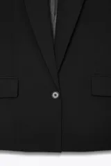 Blazer negro de corte oversize, con cuello solapa, escote pico, manga larga con hombreras y forro interior. Presenta bolsillos con solapa delanteros y bolsillo de vivo en el pecho.