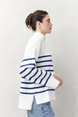 Polera blanca de punto con cuello alto y cierre metálico, de calce relajado y diseño a rayas horizontales azules.