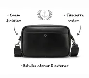 Bandolera negra de cuero sintético con correa ancha ajustable y desmontable. Cuenta con cierre superior, bolsillo frontal con tiracierre customizado, forro interno y cuatro bolsillos en total (dos exteriores y dos interiores).