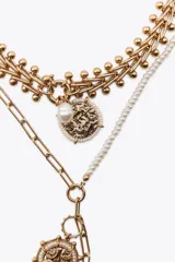 Set de tres collares dorados de diferentes largos. El primero es de eslabones con medalla labrada y perlas. El segundo combina perlas y eslabones con colgantes de medallas labradas. El tercero es de cordón con nudos y charms de diferentes formas.