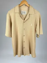 Camisa color beige claro, tejida, de manga corta, con cuello solapa y cierre frontal con botones.