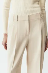Pantalón de vestir color crema, de tiro alto y pernera ancha, con pinzas delanteras, bolsillos frontales y falsos bolsillos de doble vivo en la espalda.