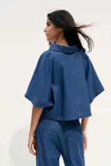 Camisa corta de denim azul, con cuello solapa, escote en pico y mangas cortas.