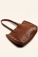 Bolso tote de cuero color marrón con doble asa de hombro y tachas plateadas en los laterales y la base. Incluye sobre interior de cuero.