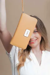 Billetera larga color mostaza con cierre alrededor, múltiples compartimentos internos, tarjetero, visor para documentos, bolsillo interno con cierre y correa de mano.