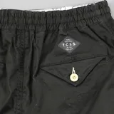 Bermuda de algodón color negro, con cintura elástica y cordón de ajuste color crema. Presenta bolsillos laterales y un pequeño parche con texto en la parte inferior derecha.