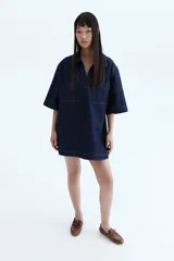 Vestido corto de denim azul oscuro, corte recto, con cuello camisero con escote en V, manga corta y dos bolsillos de parche en el pecho.