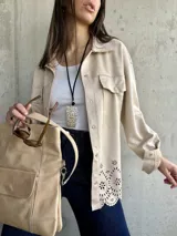 Sobrecamisa color beige de gamuza sintética, corte oversize, con cuello camisero, cierre frontal con botones a presión, bolsillos de parche en el pecho y detalle calado con motivos florales en el ruedo.