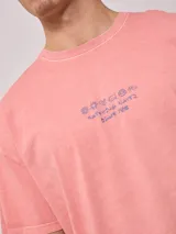 Remera de algodón con efecto lavado, color rosado, de calce oversize. Presenta un estampado grande en la espalda con un sol estilizado, el logo de Rusty y el texto "RUSTY CULTURE AUSTRALIA".