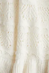Musculosa corta de punto crochet color blanco, con escote redondo pronunciado con ribete festoneado y bajo acanalado de volado. Sin mangas.