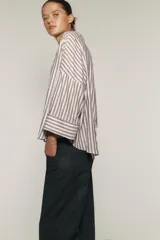 Camisa a rayas verticales color marrón y blanco, de corte holgado, con cuello solapa, cierre frontal con botones y mangas anchas por debajo del codo.
