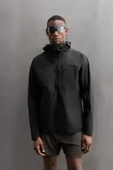 Cazadora negra de tejido técnico ripstop, con cuello alto, capucha ajustable y visera. Tiene mangas largas con puños elásticos, bolsillo de seguridad con cremallera en el pecho, bajo con elástico en los laterales y cierre frontal con cremallera.