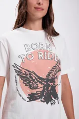 Remera blanca de algodón con cuello redondo y mangas cortas. Estampado frontal con la frase "Born to Ride" y un águila en color negro sobre un círculo rosa.