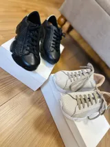 Zapatillas deportivas urbanas de cuero negro y beige con cordones y suela gruesa.